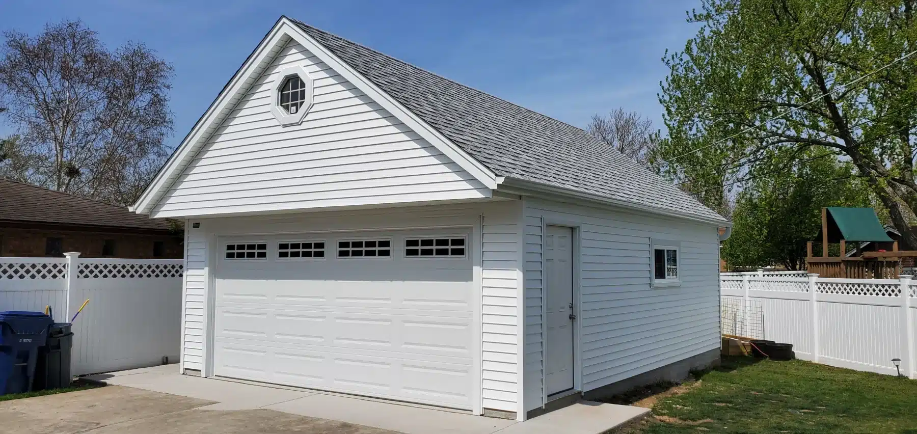 20210427_104109_resized A detached garage featuring white siding and a white roof, showcasing a gable style design in a suburban setting.